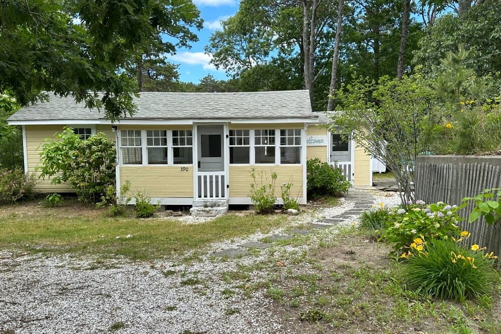 A small yellow house surrounded by greenery and a gravel driveway.