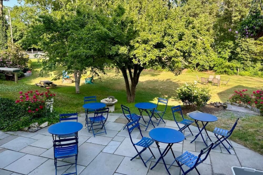 A patio with blue bistro tables surrounded by greenery and flowers.