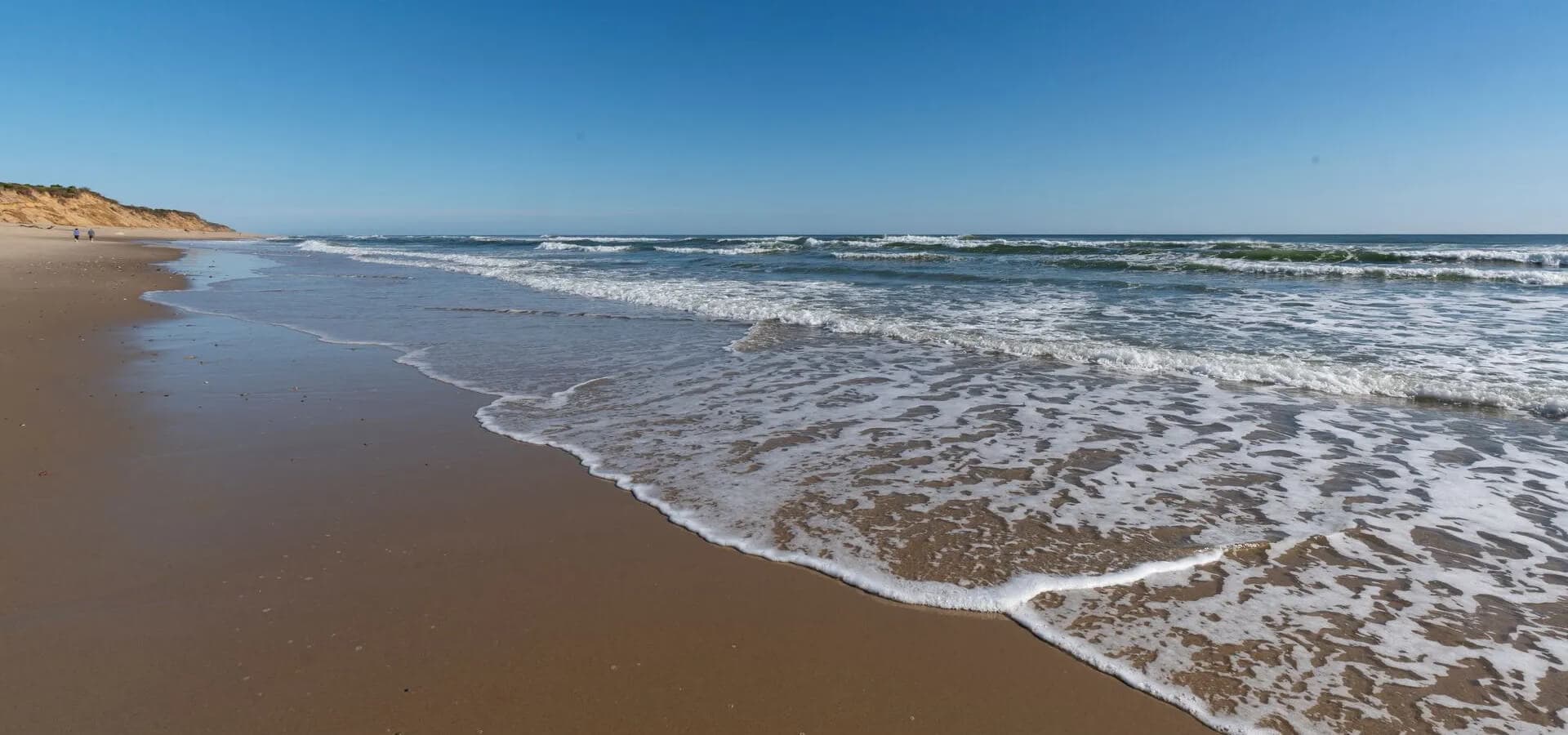 A serene beach scene with gentle waves lapping at the sandy shore under a clear blue sky.